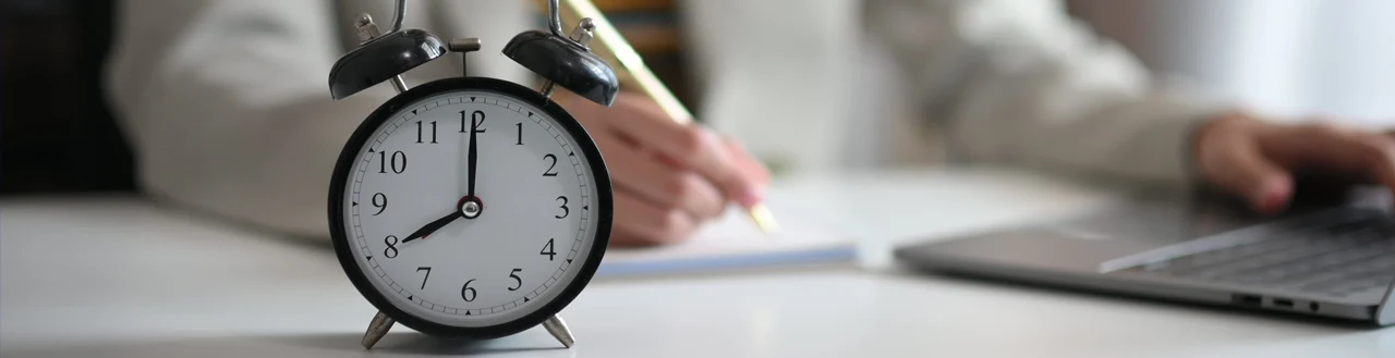 Man works with laptop on office desk with alarm clock for tracking time at work